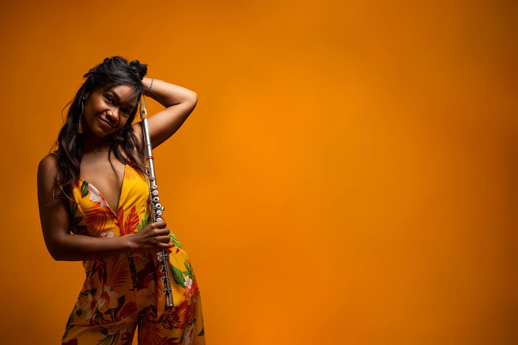 Magela Herrera smiling with her flute resting against her shoulder, against an orange backdrop