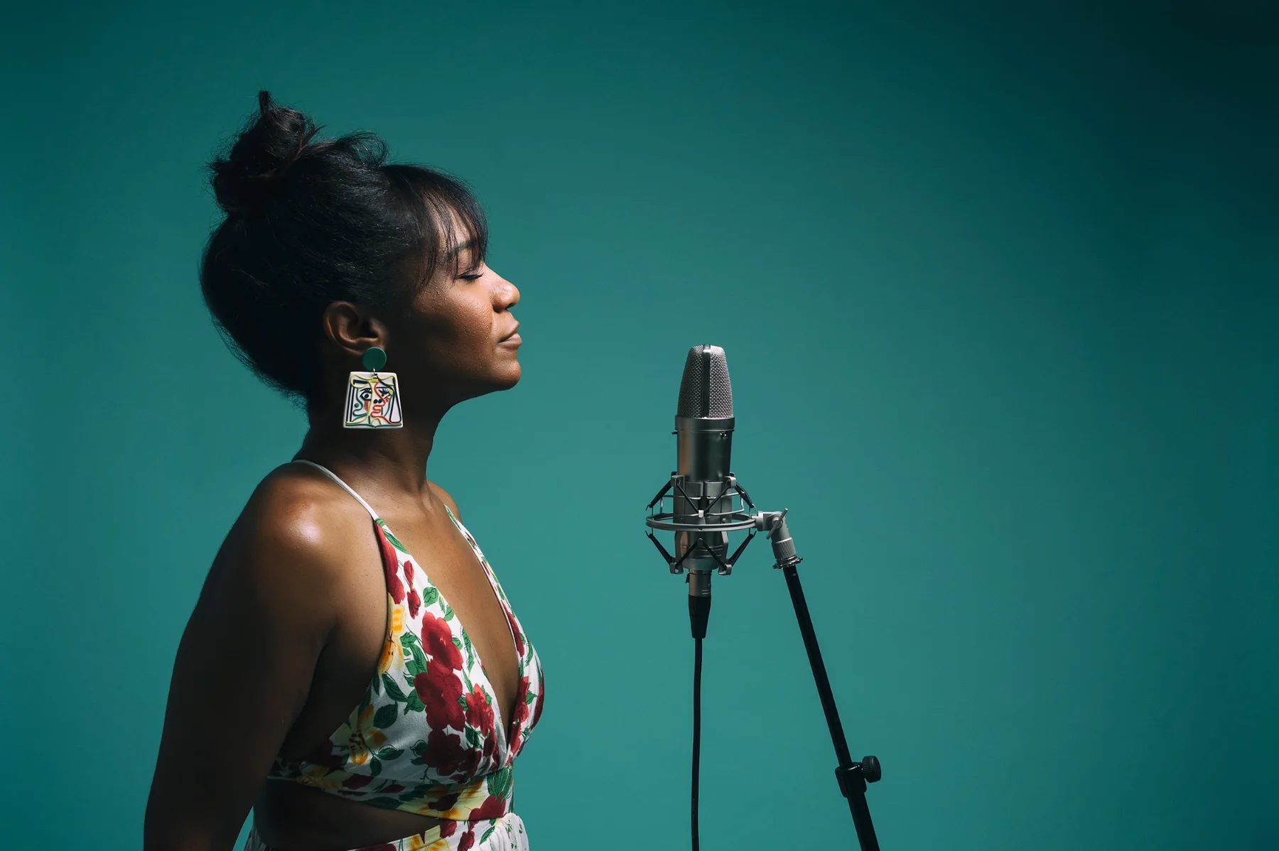 Magela Herrera in profile with eyes closed before a studio microphone, against a teal backdrop