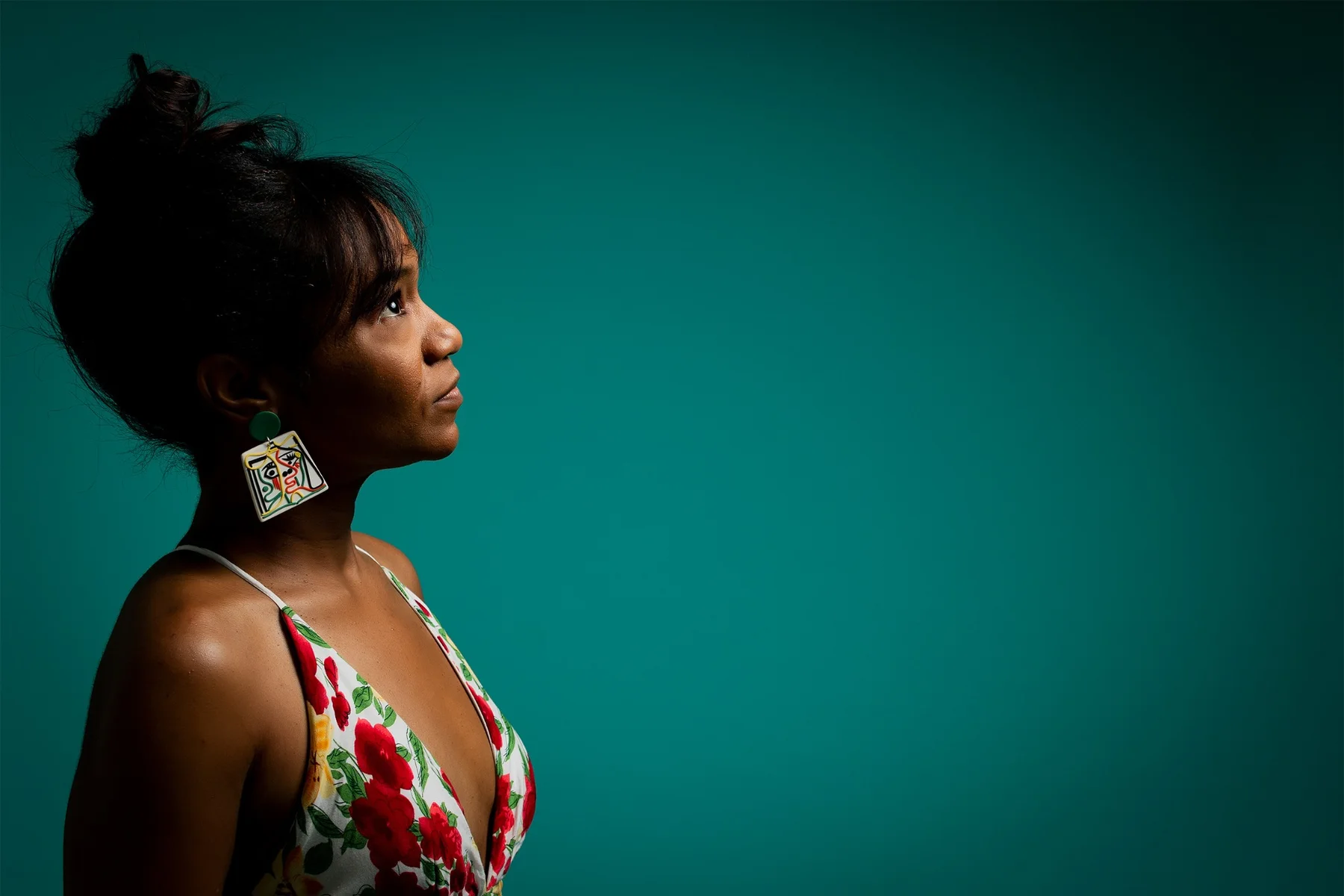 Magela Herrera in profile looking upward, wearing a floral dress against a teal backdrop